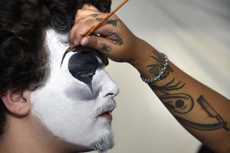 Person painting a man's face in clown makeup.